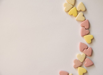 pink and yellow Vitamins in the shape of a heart lie on a white background in an orderly manner on one side framing a leaf