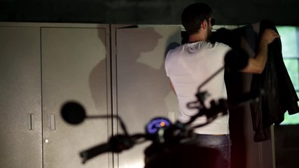  Biker in a leather jacket resting on the bike in the dark.