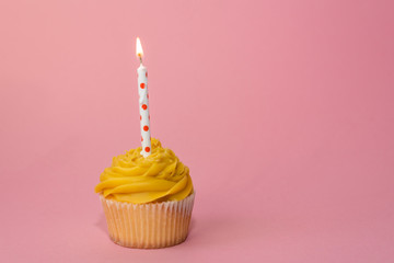 Yellow birthday cupcake with a candle, on pink background. Copy space