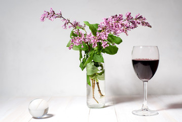 Bouquet of lilac in a vase, a glass of wine and a transparent ball