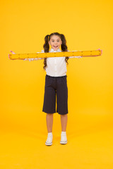 What a long ruler. Surprised little student holding rigid wooden ruler on yellow background. Small...