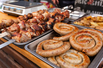 A counter with metal trays containing grilled sausages and meat. Food and cooking equipment at a street food festival