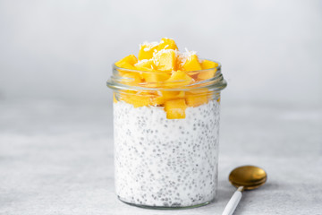 Chia seed pudding with mango and coconut in glass jar on bright grey concrete background. Healthy...
