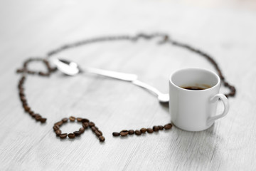 Coffee grains folded in the form of a clock on a wooden background. Instead of the number 7, a cup...
