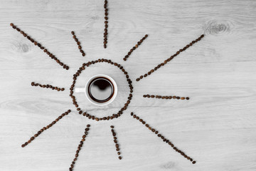 Coffee grains folded in the form of the sun on a wooden background. In the middle is a cup of...
