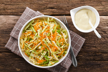 Coleslaw made of freshly shredded white cabbage and grated carrot with homemade mayonnaise-based salad dressing on the side, photographed overhead (Selective Focus, Focus on the salad)
