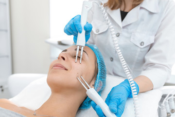 Beautician procedure of microcurrent therapy of the patient's face. A young girl is undergoing a course of spa treatments in the office of a beautician. Moisturizing, cleaning and facial skin care. 