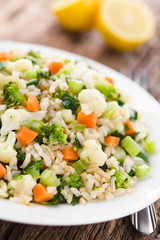 Fresh cooked brown rice with steamed vegetables (broccoli, cauliflower, swiss chard, carrot, celery) on plate, lemon in the back (Selective Focus, Focus one third into the plate)