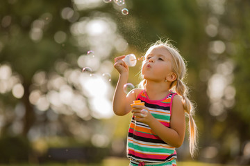 little blonde girl inflates soap bubbles in summer on a walk,  International children's day
