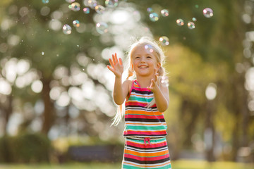 little blonde girl inflates soap bubbles in summer on a walk,  International children's day