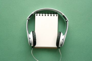Song lyrics mockup. Music playlist. Blank page notepad and headphones on a green flat lay...