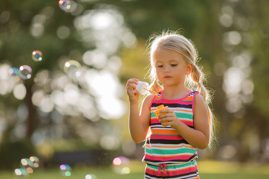 little blonde girl inflates soap bubbles in summer on a walk,  International children's day
