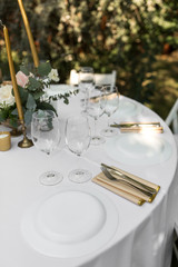 Wedding table setting decorated with fresh flowers in a brass vase. Wedding floristry. Banquet table for guests outdoors with a view of green nature. Bouquet with roses, eustoma and eucalyptus leaves