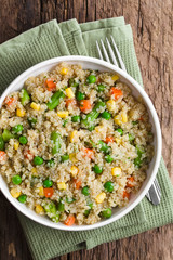 Fresh homemade cooked white quinoa with colorful vegetables (green peas, sweet corn kernels, green beans, carrots) and parsley in bowl, fork on the side, photographed overhead