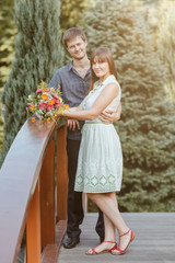 The groom makes an offer to the bride, the engagement of two young people. Beautiful girl in a summer dress with a bouquet in her hands in the park