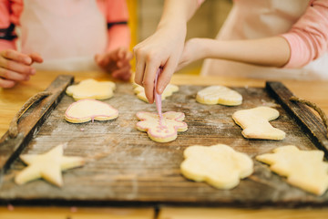 Two little girls cooks spread out cookies on board