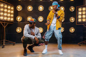 Rappers in caps dance on stage with spotlights