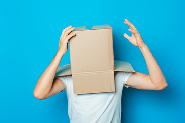 Young man in a white T-shirt with a cardboard box on his head makes a gesture with his hands on a...