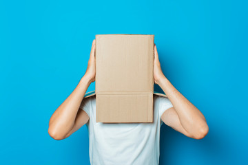 Young man in a white T-shirt with a cardboard box on his head makes a gesture with his hands on a...