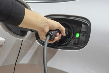 Close-up left men hands who are fueling a new vehicle electrification via rechargeable electricity machine, Electric cars are a new innovation in the future, built to replace cars powered by oil.