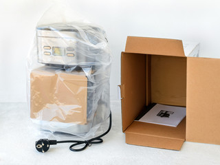 Drip-type coffee maker is in cellophane and near its cardboard box with instruction manual. Unpacking a new coffee machine. Home electrical appliances.
