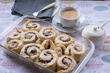 Homemade Chelsea buns in a glass dish with cup of tea