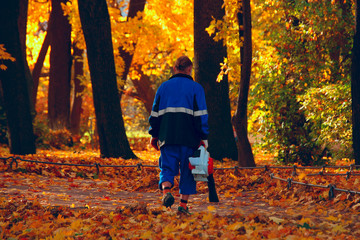 man cleaning fallen leaves with a blower in an autumn city park