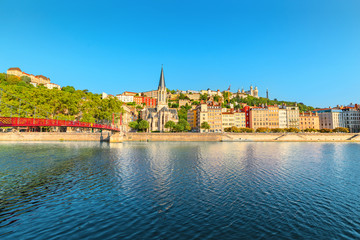 Fototapeta na wymiar Early morning cityscape view of St Georges pedestrian bridge in Lyon city with old church on the opposite bank of the river. Travel destinations in France