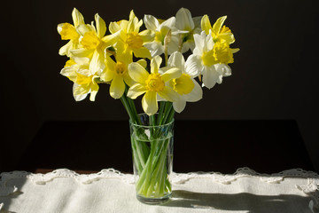 The varietal bouquet of yellow daffodils in a in a glass vase on a dark background.