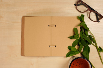 An open notebook made of kraft paper with herbs, glasses and a cup of tea on the side of a bright...