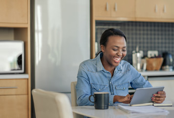 Laughing African American woman using a tablet in her kitchen