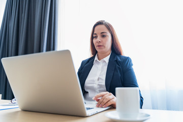 Young attractive caucasian woman smiling and making video call or online chat, looks at web camera of laptop. Distant teacher or coach, or tutor of online school or internet friend