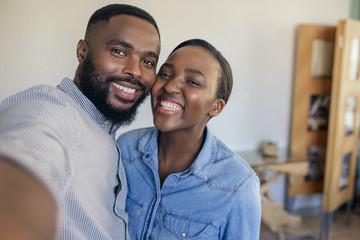 Smiling young African American couple taking a selfie at home