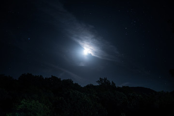 Mountain Road through the forest on a full moon night. Scenic night landscape of dark blue sky with moon.