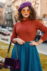 Outdoor autumn portrait of young beautiful elegant lady wearing wrist watch, purple beret, orange...