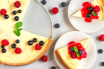 cheesecake with two slices of cake with fresh raspberries, blueberries, jam and mint on marble background. top view