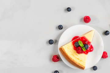 slice of classical cheesecake with fresh raspberries, blueberries, jam and mint on marble background. top view
