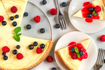 classic New York cheesecake with two slices of cake in plates with fresh berries, jam and mint on...