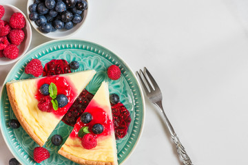 two slices of cheesecake with fresh raspberries, blueberries, jam and mint in a blue plate on marble background. top view
