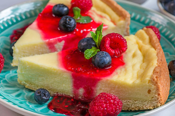 two slices of classic New York cheesecake in a blue plate with fresh berries, jam and mint