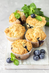 Blueberry muffins with fresh berries and mint leaves on light grey stone background. Copy space.
