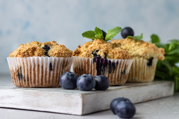 Blueberry muffins with fresh berries and mint leaves on light grey stone background. Copy space.