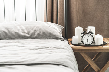 Cozy gray bedroom interior with comfortable bed near the wooden night table with candle, alarm clock and dried flowers. Cozy atmosphere at home. Warming up autumn evenings. Vintage furniture.