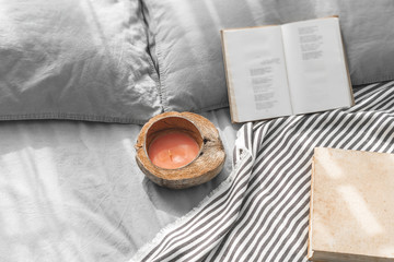 Cozy messy bed with two pillows, gray bed linen with books and coconut shell candle.  Cozy atmosphere at home. Warming up the cold winter or autumn evenings. Vintage furniture.