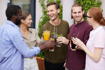 Multi-ethnic group of people enjoying cold drinks and chatting cheerfully during outdoor Summer party