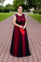 Fototapeta premium Brunette caucasian model in floor-length black and red dress with embroidery in park.