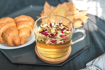 Cozy autumn morning concept. Breakfast with herbal tea and croissants on the bed with grey sheets in a sunny room