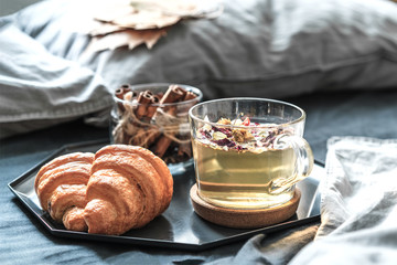 Cozy autumn morning concept. Breakfast with herbal tea and croissants on the bed with grey sheets in a sunny room