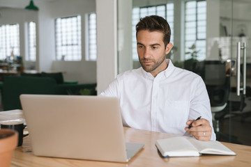 Young businessman writing down notes while working on a laptop