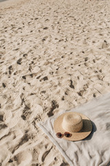Tropical beautiful beach with white sand, foot steps, neutral blanket with straw hat and sunglasses. Relaxing atmosphere. Summer travel or vacation concept. Minimalistic background.